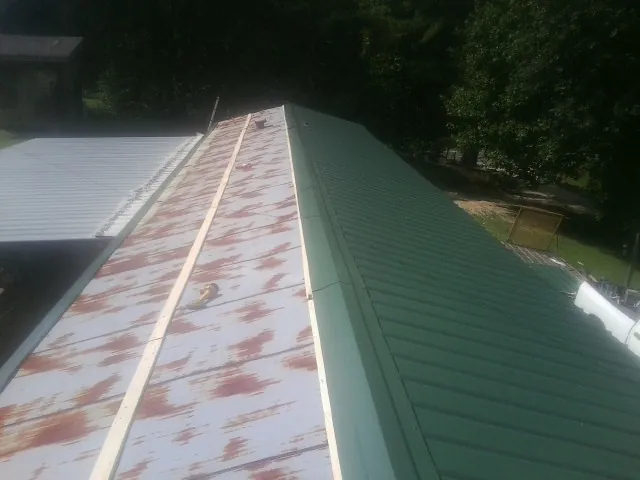 Old rusted panels beside newly installed green metal roofing — Wind Damage Roof Repair by Roofing Brothers in Elizabethport