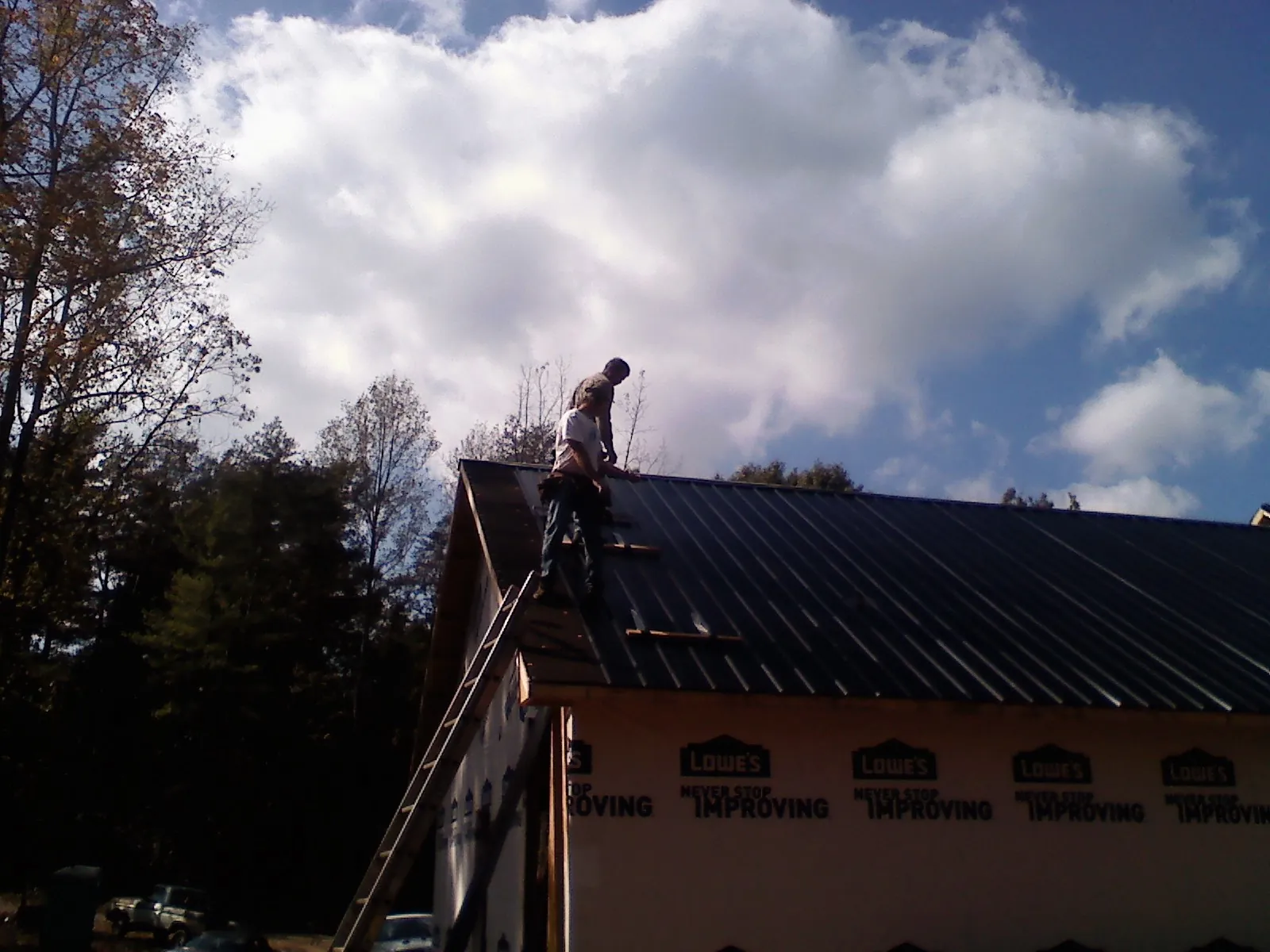 Roofer fastening dark metal panels high against a cloudy sky, from a Roof Inspection job in Elizabethport