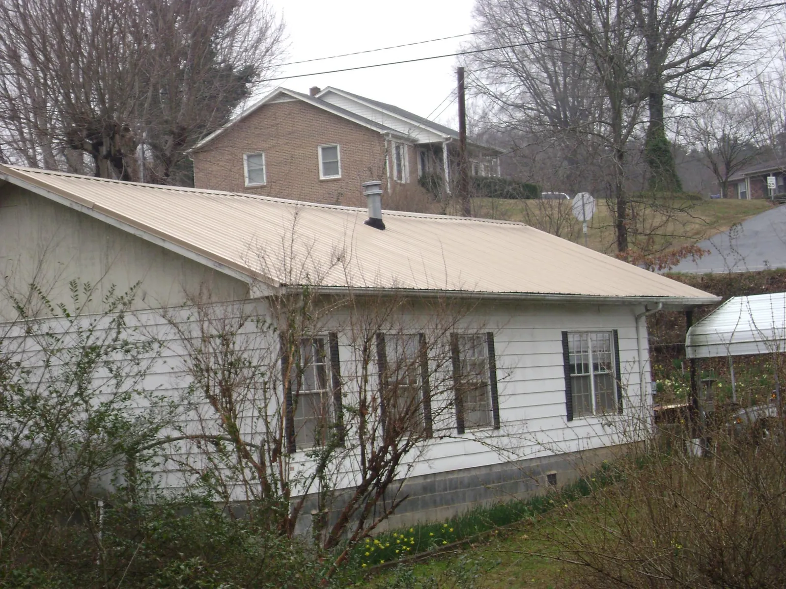 Tan metal roof on a white sided house set into a hillside — Commercial Roofing by Roofing Brothers in Elizabethport
